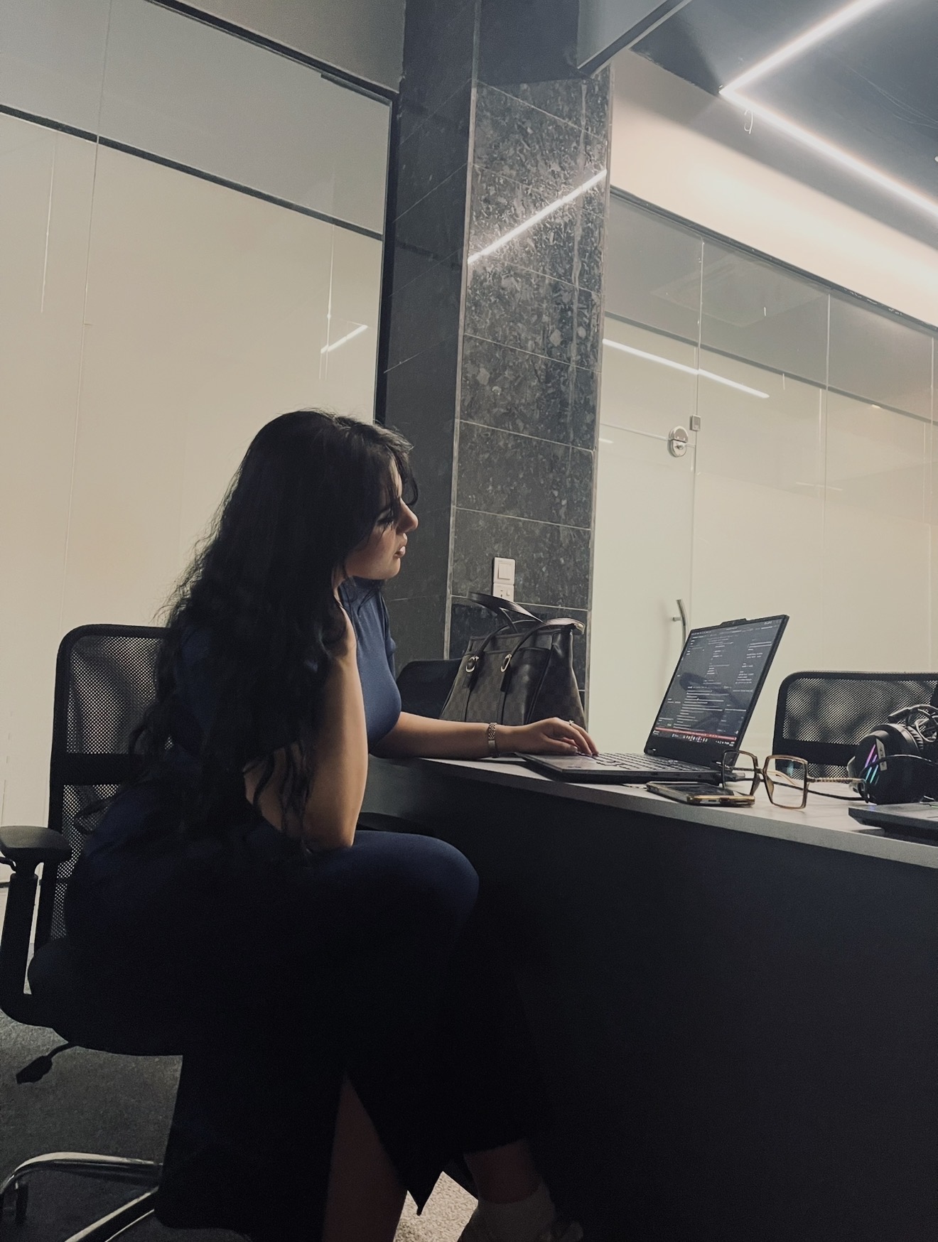 Shahad Haider working at her laptop in a modern glass-walled office, reviewing code on screen